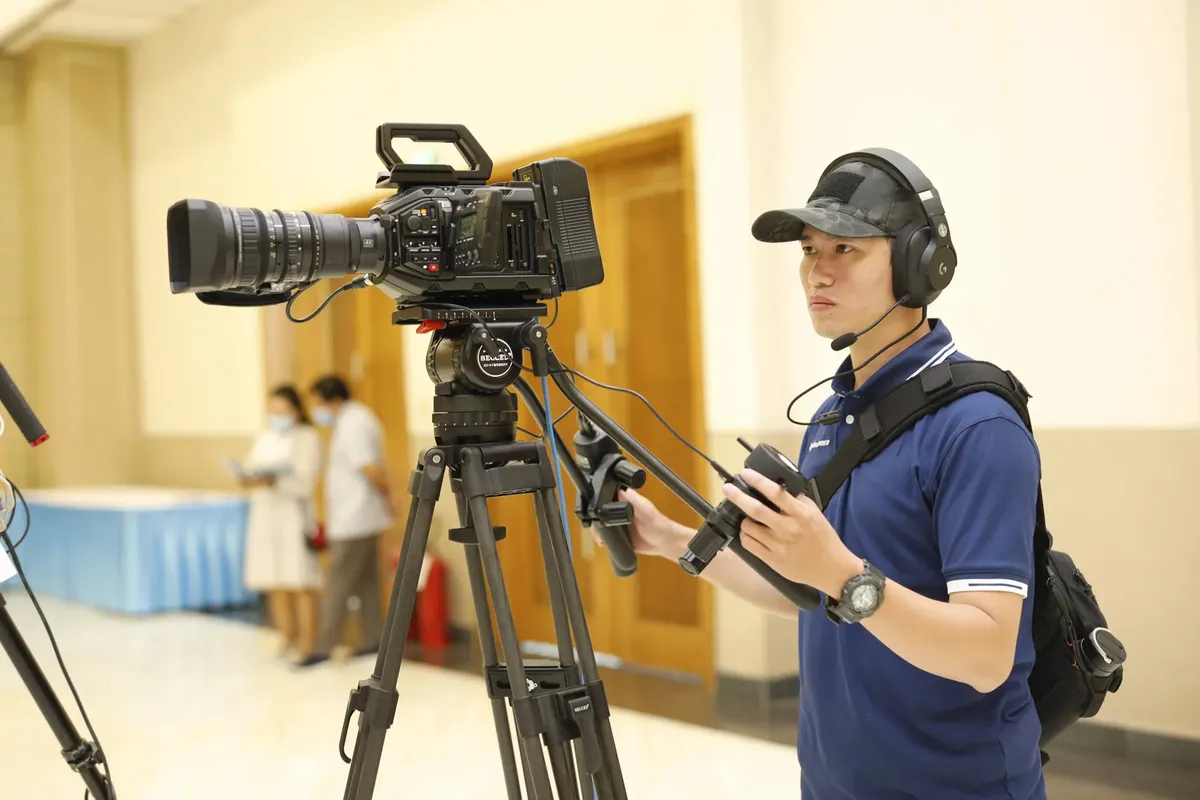 Cameraman capturing footage with professional video camera on tripod. Indoor setting, focused on technology.