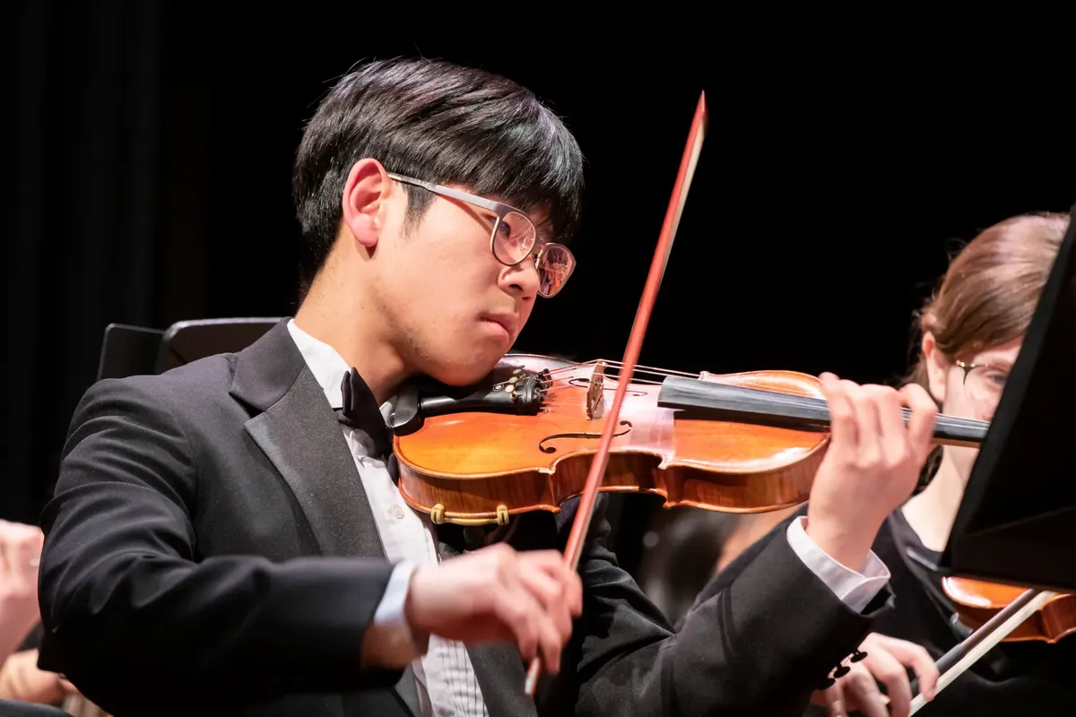 Close-up of an Asian violinist passionately playing on stage during a live performance.