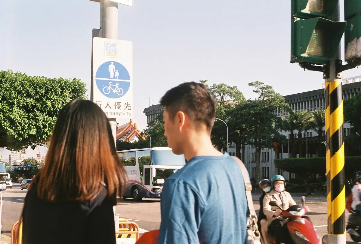 Street view in Taiwan featuring pedestrians, cyclists, and traffic at a crosswalk on a sunny day.
