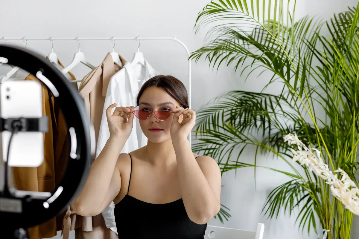 スタイlishな女性がサングラスをかけたまま室内でファッションコンテンツを録画している